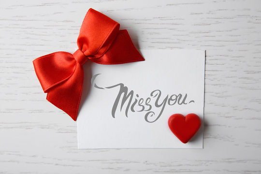 Blank present card with ribbon bow and small heart on wooden background