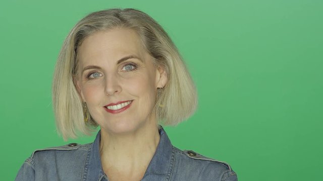 Beautiful older woman smiling and being playful, on a green screen studio background