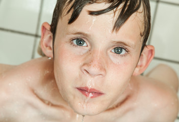 Young boy taking a shower under running water