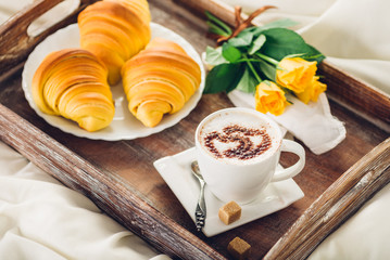 Coffee, croissant and flowers on tray on a wooden table