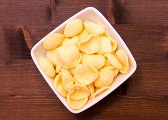 Potato snacks on a square bowl on wooden table seen from above