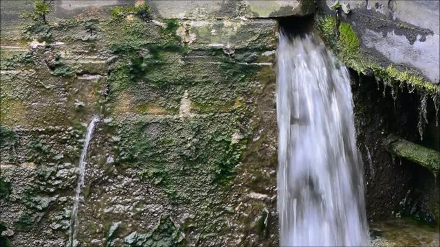 Water spilling through leaking wall of canal lock. Lock with water escaping at high pressure through gaps in brickwork, splashing onto cill