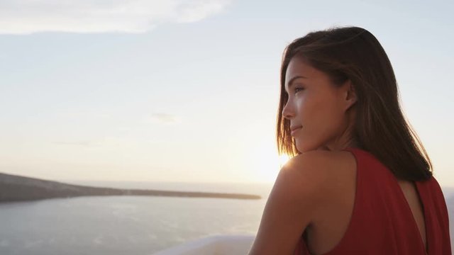 Beautiful woman enjoying the beautiful view of Aegean Sea during sunset. Female tourist is wearing red dress while standing at caldera. She is on her vacation in Santorini.