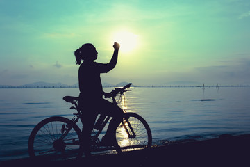 Fototapeta premium Silhouette of happy female celebrating with arm up towards the sun