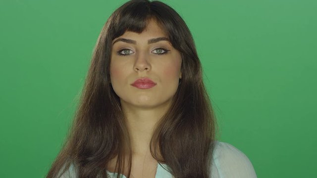 Beautiful brunette woman staring and smiling, on a green screen studio background