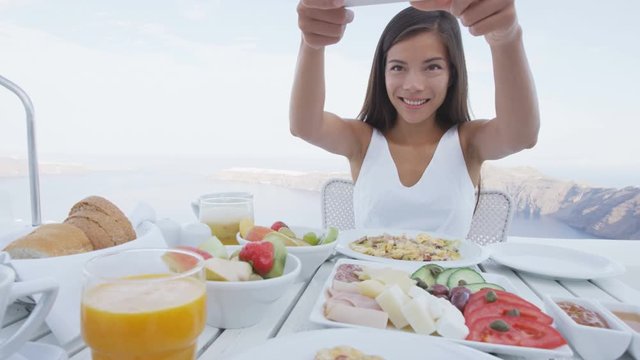 Woman taking photo of breakfast using mobile cell smart phone app. Girl taking pictures of food on luxury travel vacation for social media. Beautiful female in resort in Santorini, Greece, Europe.