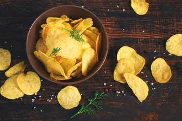 Fotobehang Crispy potato chips in a cup on a dark background, tinted © colnihko