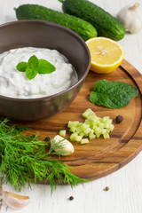 Tzatziki sauce in a bowl and ingredients - cut cucumber, mint, d
