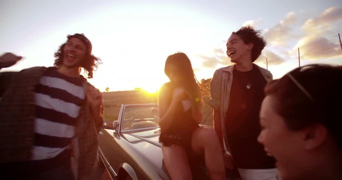 Teenage boho friends embraging and laughing at sunset
