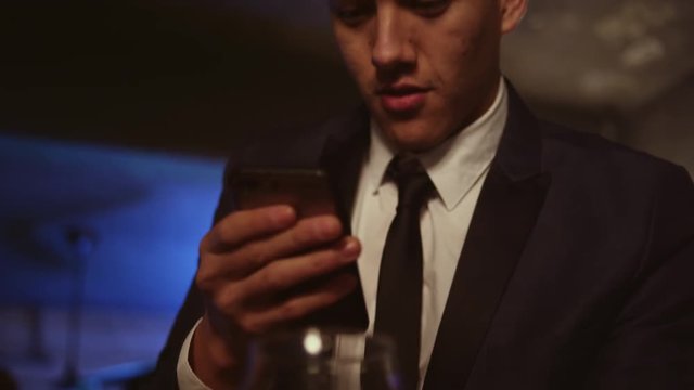 Well dressed young man in a nightclub taking a picture of his drink with his cell phone