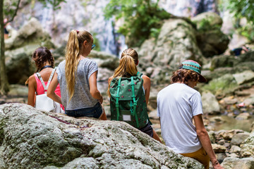 Young tourists are resting on the rocks in the jungle waterfall in the background