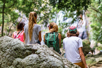 Young tourists are resting on the rocks in the jungle waterfall in the background