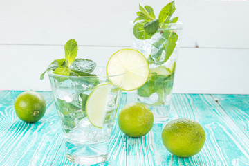 mojito in glasses with ice cubes,  decorated by mint leaf, lime fruits on turquoise colored wooden table