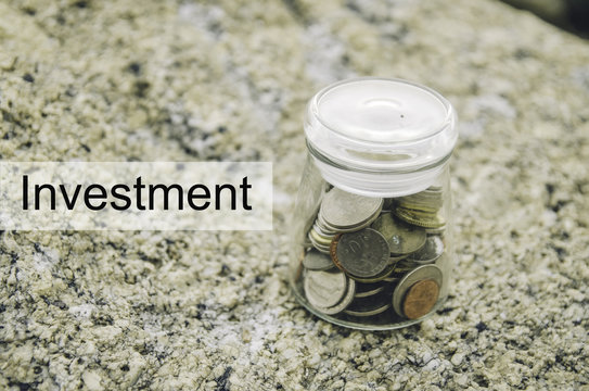 Financial image concept with word INVESTMENT. Blurred background coin in glass jar on the rock.