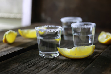 stack of tequila with salt and lemon on a wooden background