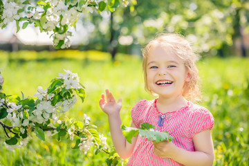 Happy little girl playing in spring apple tree garden