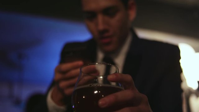 Well dressed young man in a nightclub taking a picture of his drink with his cell phone, close up