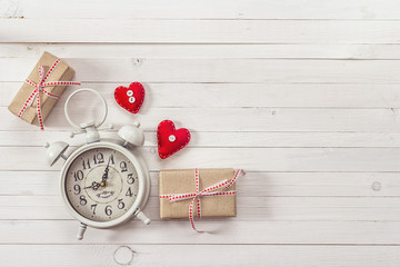 Background with white alarm clock, gift boxes and red hearts on