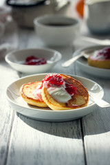 Summer cottage cheese pancakes on white plates on a wooden table with coffee, milk, sour cream and jam, closeup, toned, selective focus.