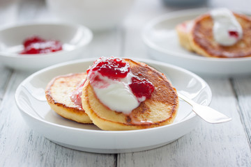 Summer cottage cheese pancakes on white plates on a wooden table with coffee, milk, sour cream and jam, closeup, selective focus.