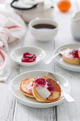 Summer cottage cheese pancakes on white plates on a wooden table with coffee, milk, sour cream and jam, closeup, selective focus