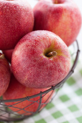 Fresh red juicy apples in a basket on a green textile on a wooden background, closeup.