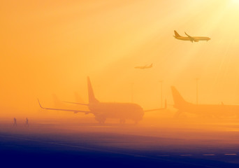Airport in a foggy weather - silhouettes of airplanes early in the morning. Aircrafts in a fog, international airport at sunrise. Air travel - passenger and commercial transportation.