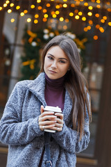 Beautiful smiling woman  holding a cup of coffee in her hands in the city