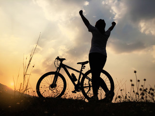 Obraz premium Silhouette women showing her hands with bicycle at sunset