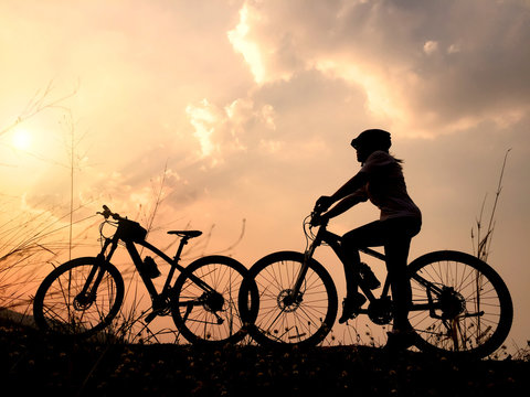 Silhouette women ride bicycle at sunset