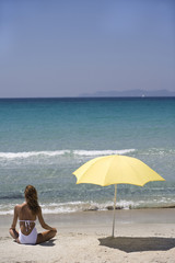 femme assise de dos à la plage à coté d'un parasol