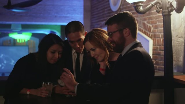 A group of friends in a nightclub looking at pictures on a cell phone and laughing