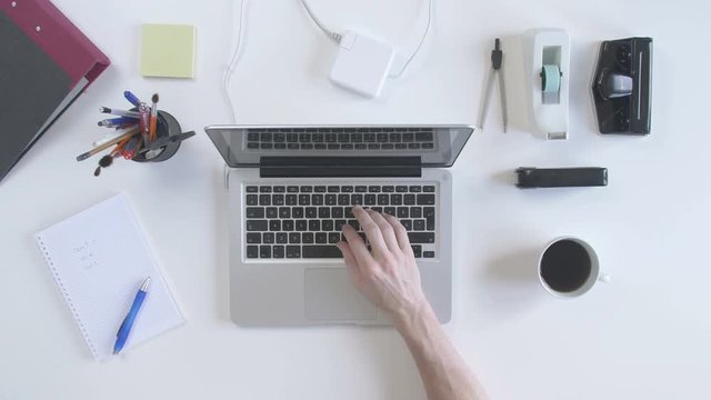Top view of desk with office supplies. Man taking a break from typing on his laptop. Lay down his glasses and drink coffee
