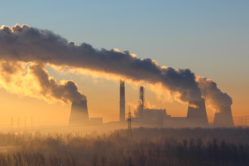 Foggy landscape: the power plant with huge cooling towers with thick clouds of smoke on a background of dawn, morning fog and trees 