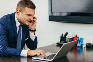 Businessman in modern office, working on laptop, talking over the phone