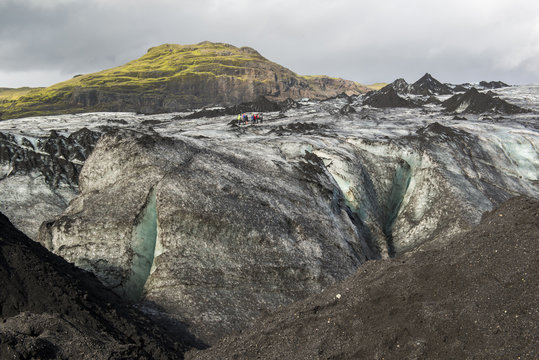 Solheimajokull glacier covered with black volcanic ash with blue cleft and group of hiking people, South Iceland