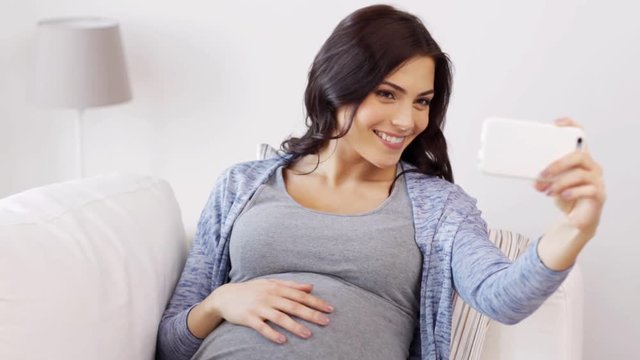 pregnant woman taking selfy by smartphone at home