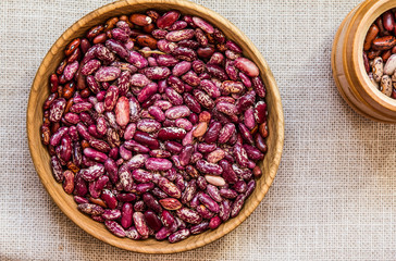 Raw colorful beans in a wooden plate and a wooden jar on linen napkin