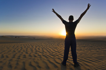 Fototapeta na wymiar standing man with hands up at sunset in desert