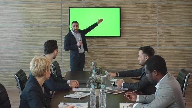 Businessman standing in front of his colleagues with microphone and presenting his project on TV with green screen