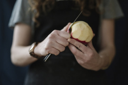 A woman in a blue apron peeling an apple with a knife.