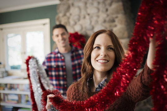 A young couple hanging tinsel up, decorating a house at Christmas. 