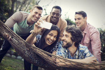 A group of friends lounging in a large hammock in the garden having a beer, and taking a selfie. 