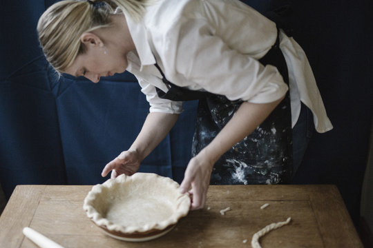 A woman working smoothing the edge of a pastry case lining a pie dish. 