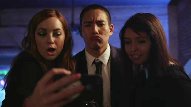 Three well dressed friends in a nightclub taking selfies with a cell phone