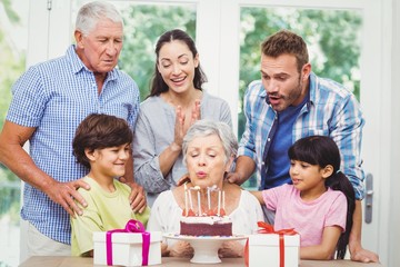 Fototapeta premium Granny blowing birthday candles with family 