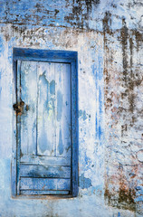 Blue grungy wooden door on dirty stone building.