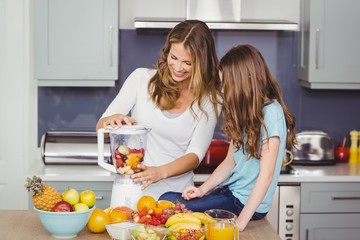 Happy mother and daughter preparing fruit juice