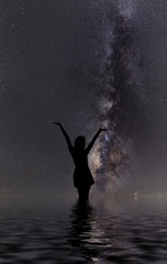 Fototapeta premium Silhouette of woman standing next to the milky way and pointing on a bright star.