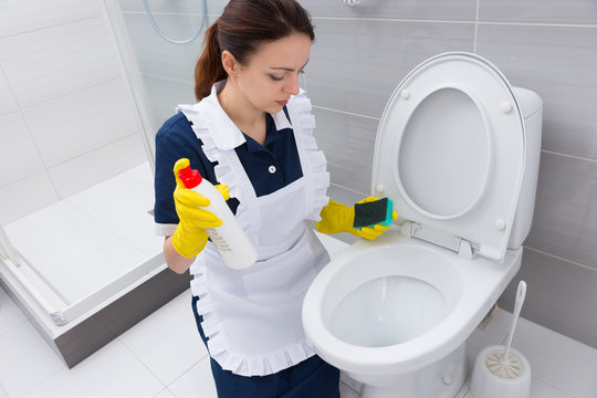 Housekeeper with sponge and cleaner at toilet